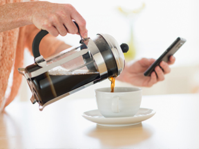 A Person Pouring a Cup of Coffee While Using Mobile Device